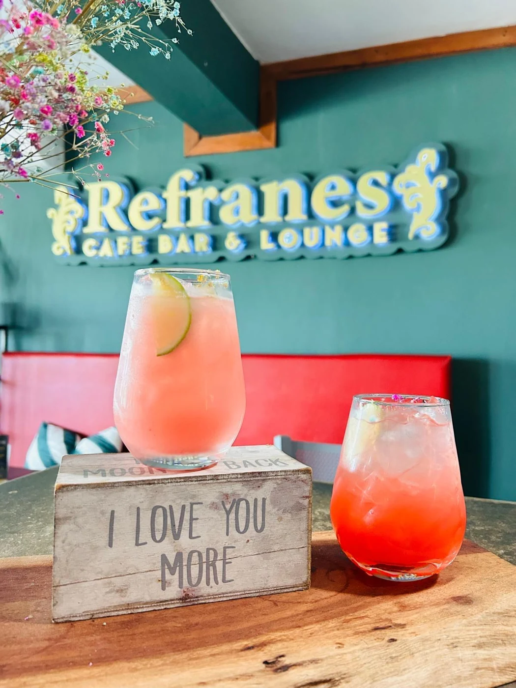 Dos bebidas frente al letrero de Refranes en el salón de paredes verdes