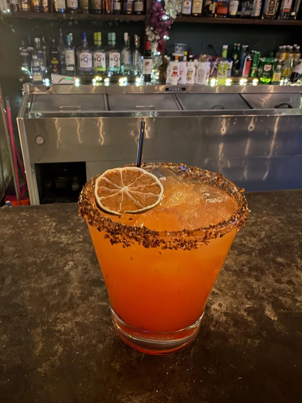Cóctel anaranjado con rueda de cítrico en la barra